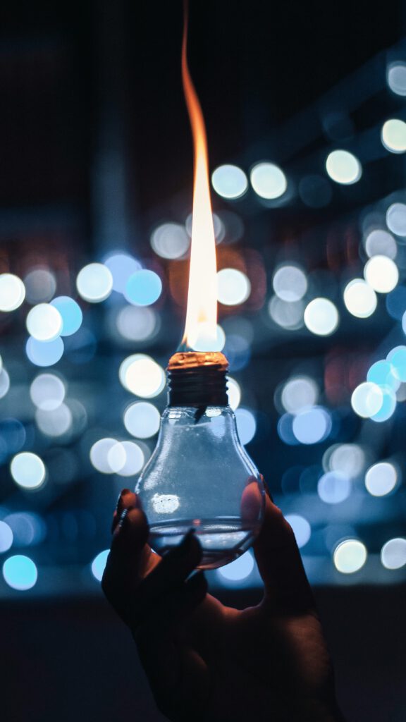 A hand holds a light bulb with a unique flame effect against a glowing bokeh backdrop.